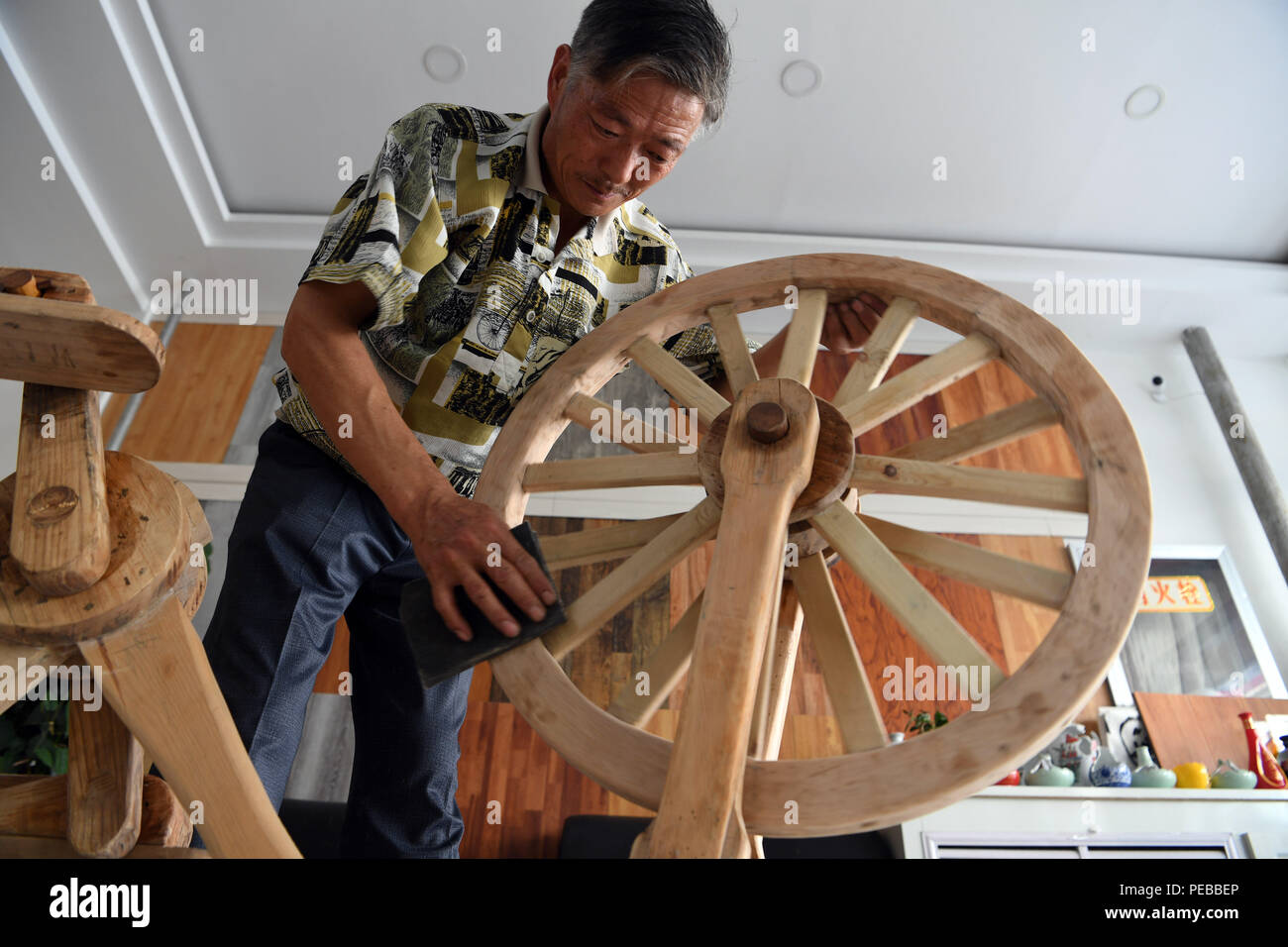 Pingliang, China's Gansu Province. 14th Aug, 2018. He Yong polishes the wheel of a wooden bicycle in Liuhu Township of Pingliang City, northwest China's Gansu Province, Aug. 14, 2018. The 55-year-old farmer He Yong successfully made a 1.8-meter-long and 0.98-meter-high wooden bicycle in 2017. The bike was made purely of wood, including walnut and elm. Credit: Fan Peishen/Xinhua/Alamy Live News Stock Photo