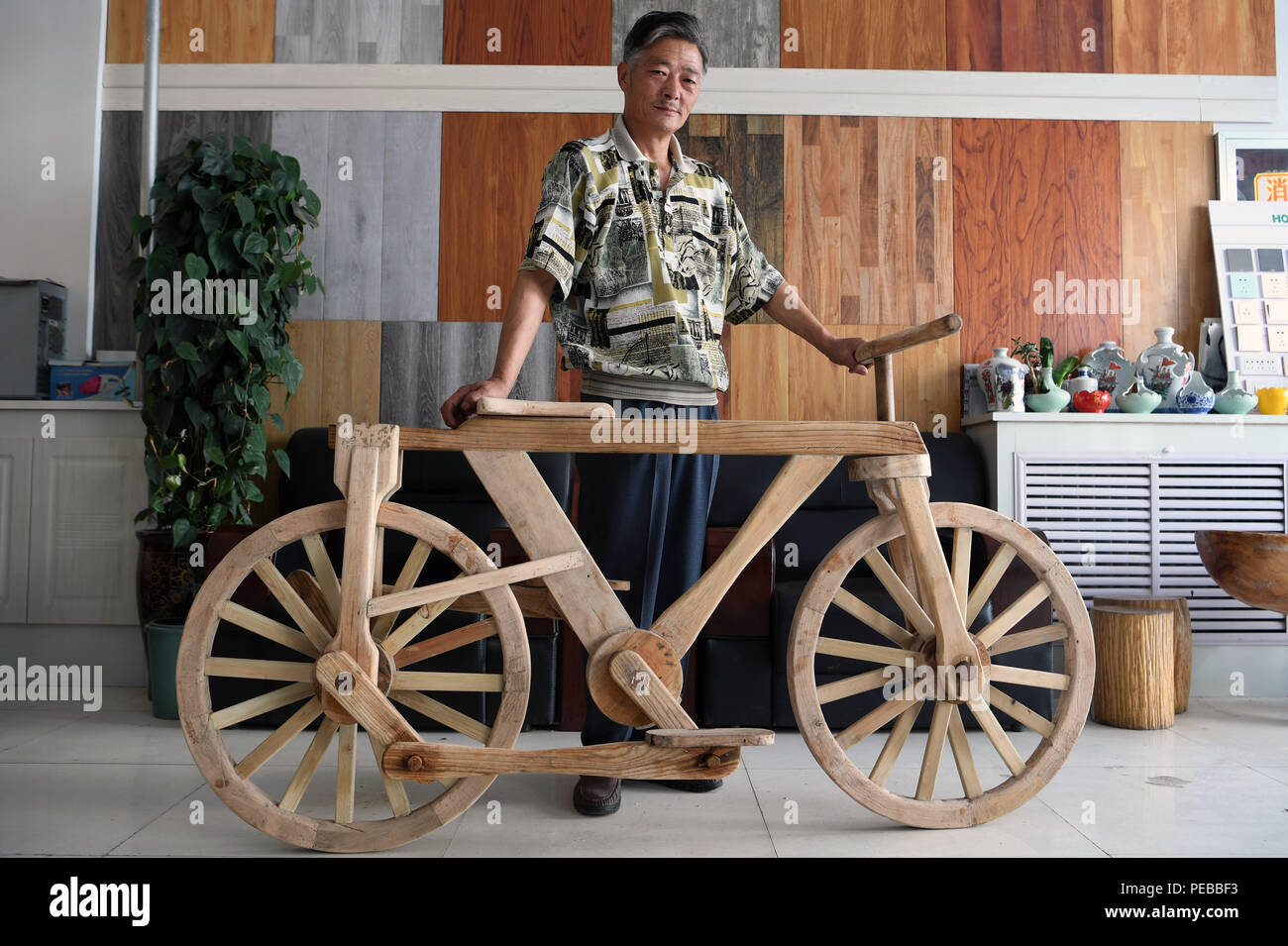 Pingliang, China's Gansu Province. 14th Aug, 2018. He Yong shows his wooden bicycle in Liuhu Township of Pingliang City, northwest China's Gansu Province, Aug. 14, 2018. The 55-year-old farmer He Yong successfully made a 1.8-meter-long and 0.98-meter-high wooden bicycle in 2017. The bike was made purely of wood, including walnut and elm. Credit: Fan Peishen/Xinhua/Alamy Live News Stock Photo