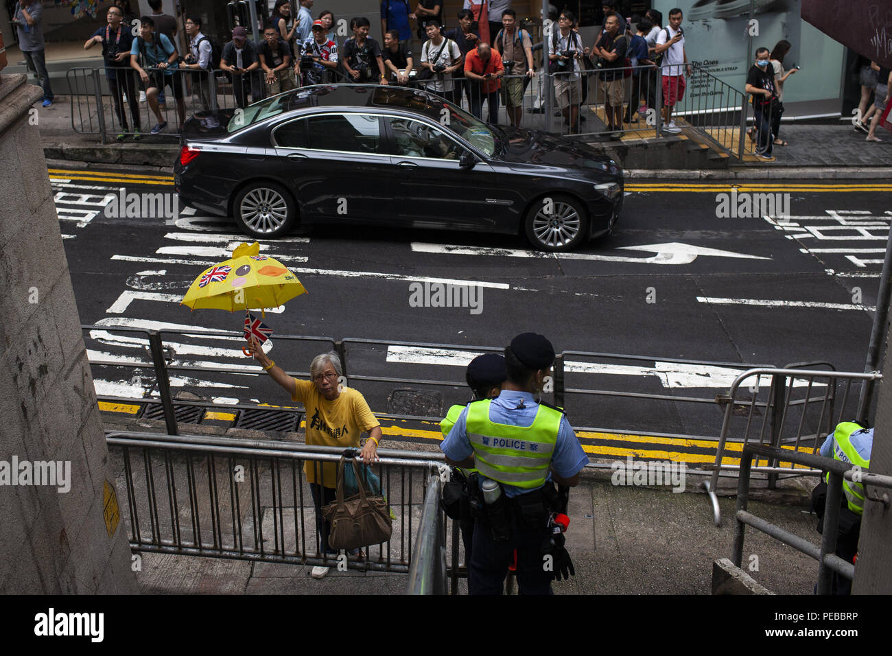 August 13, 2018 - Hong Kong, China - A Hong Kong woman wearing yellow, the color of Hong Kong Independence, hold her British umbrella high outside the back entrance to the FCC. ..Two opposing groups gather outside the Foreign Correspondents Club in Hong Kong, one in support of its hosting a talk with Independent Party leader Andy Chan, and the other - in opposition. Hong Kong is taking measures to legally eliminate the party. (Credit Image: © Viola Gaskell/SOPA Images via ZUMA Wire) Stock Photo