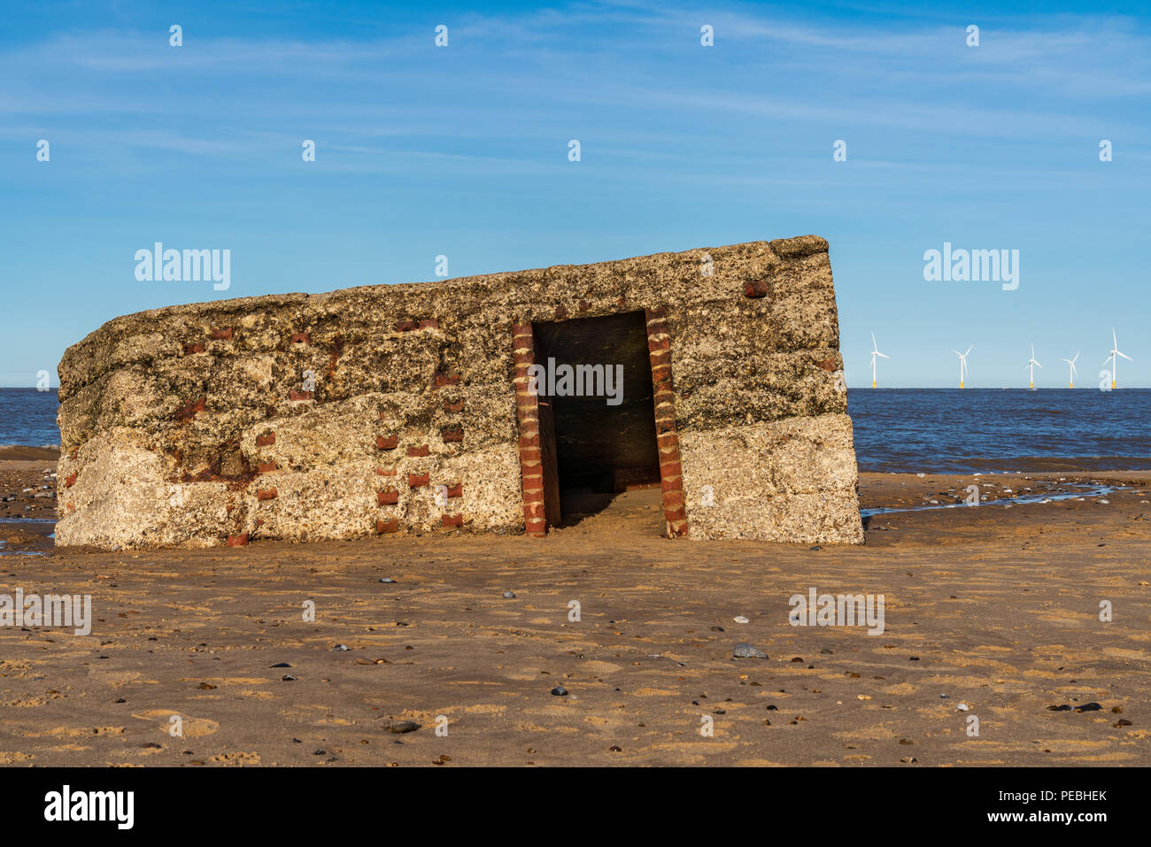 North sea coast in Caister-on-Sea, Norfolk, England, UK -  with an old bunker on the beach and wind turbines in the background Stock Photo