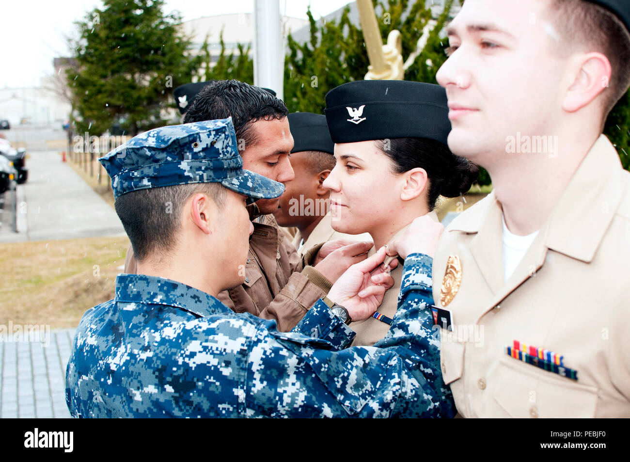 151201-N-EC644-028 MISAWA, Japan (Dec. 1, 2015) Aviation Maintenance Administrationman 3rd Class Sheila Gomez, from Caguas, Puerto Rico, has her third class collar devices pinned on by her husband, Ivan Gomez, background, and Aviation Maintenance Administrationman 1st Class Xiaojie Huang, left, during a frocking ceremony at Naval Air Facility Misawa. (U.S. Navy photo by Senior Chief Mass Communication Specialist Ryan C. Delcore) Stock Photo