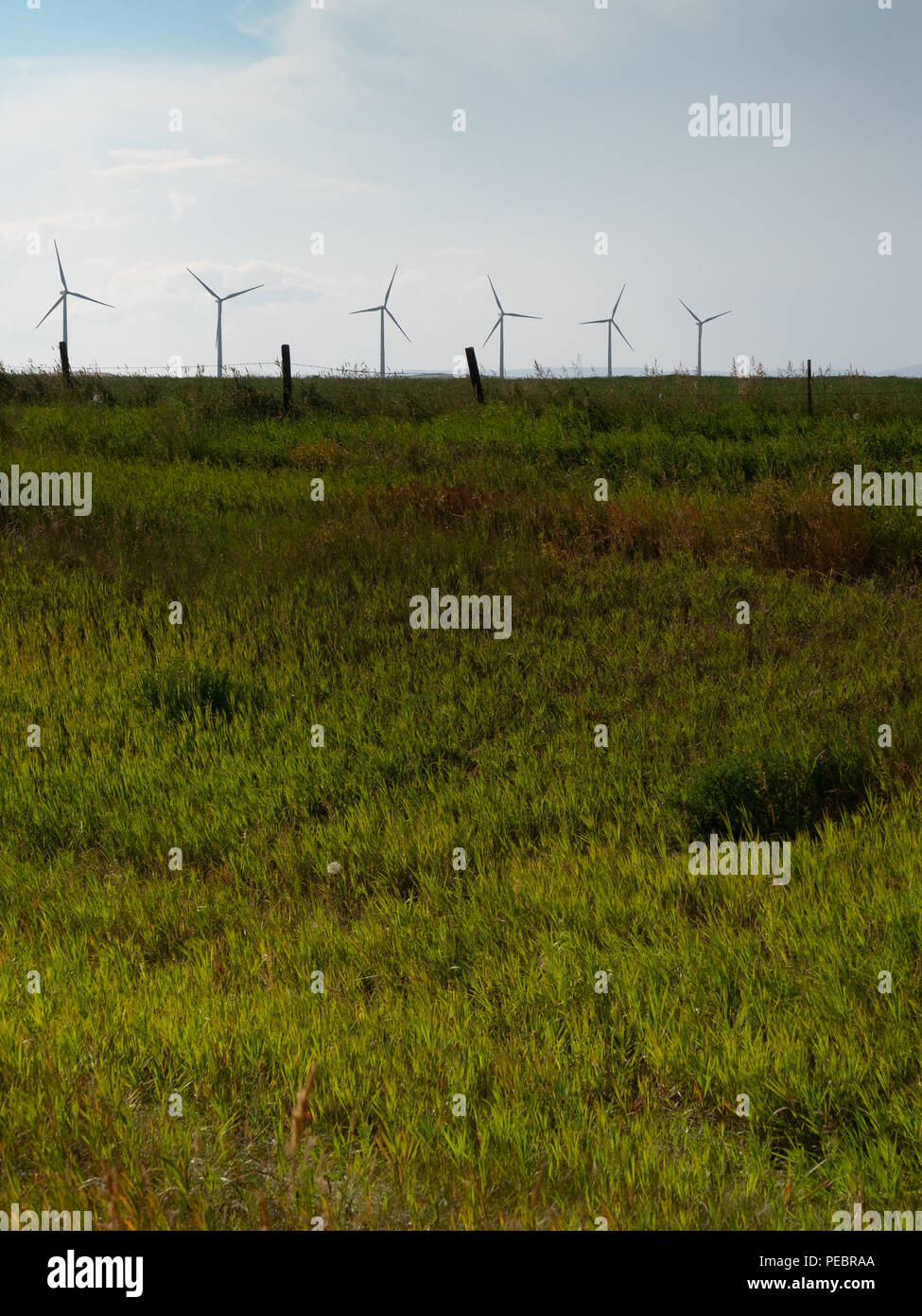 Six windmills on the crest of a hill with a lush, grassy meadow in the foreground and blue sky with cirrus clouds overhead. Stock Photo