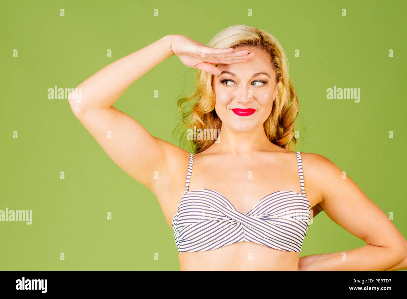 Close up portrait of a happy blonde woman in bikini with  hand by her forehead, isolated on green studio background Stock Photo