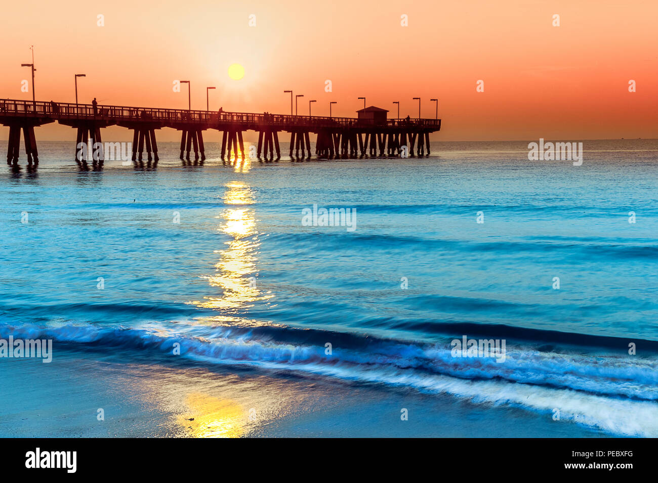 Oceanscape of the Pompano Pier and the Atlantic Ocean early morning during surise. Light surf, blue water and an orange sky on the ocean. Stock Photo