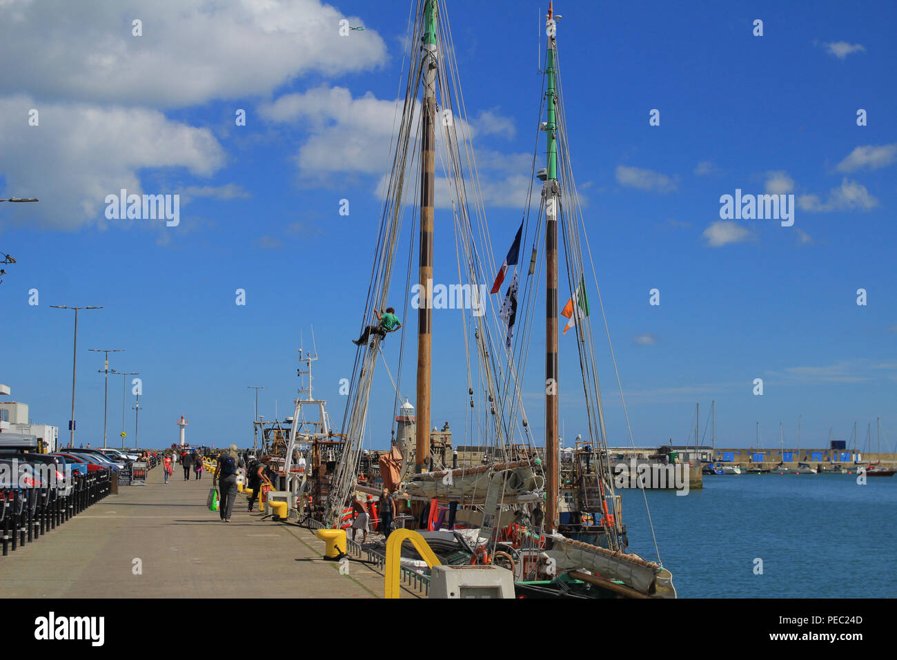 A busy morning on the west Pier Howth, Ireland with people stroling the pier and a man repairing the rigging ropes on a visiting french sail ship. Stock Photo
