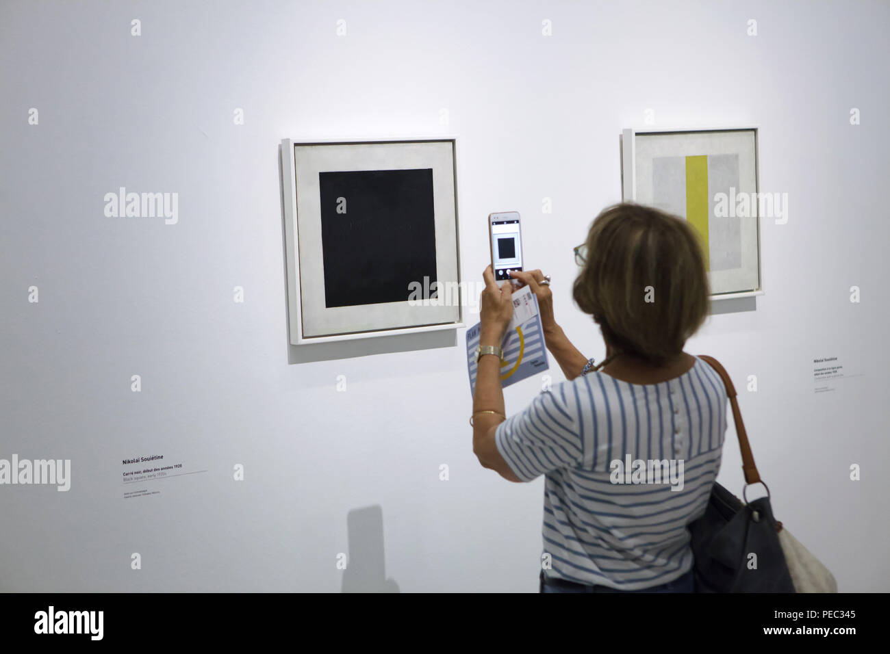Visitor uses a smartphone to photograph the painting 'Black Square' by Russian avant-garde painter Nikolai Suetin dated from the early 1920s displayed at the exhibition in the Centre Pompidou in Paris, France. The painting is a copy after the famous painting by Russian avant-garde painter Kazimir Malevich. Painting by Nikolai Suetin entitled 'Composition with a Yellow Stripe' from the early 1920s is seen in the picture at the right. The exhibition devoted to the Russian avant-garde in Vitebsk (1918-1922) runs till 16 July 2018. Stock Photo