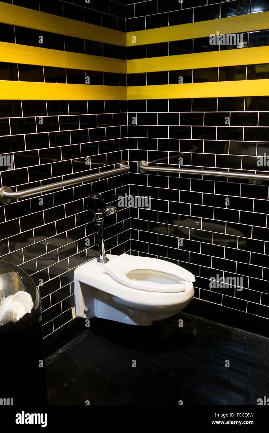 A commode in a public restroom at Third Man Records in Detroit, Michigan.  Black tile walls with yellow strips, and rails to aid handicapped. Stock Photo