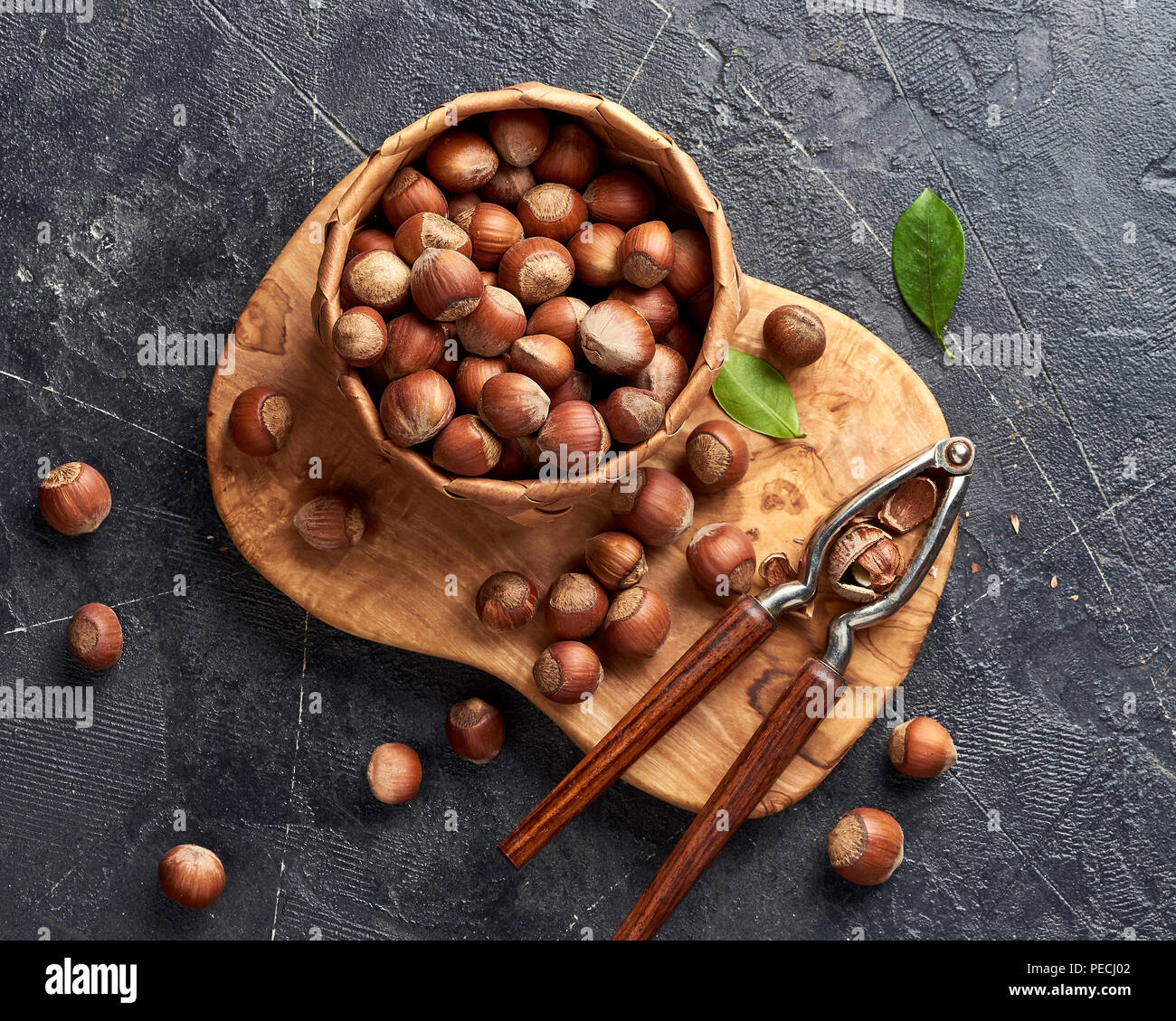 Hazelnut with nutcracker on olive wooden board. Nuts with green leaves. Top view. Stock Photo