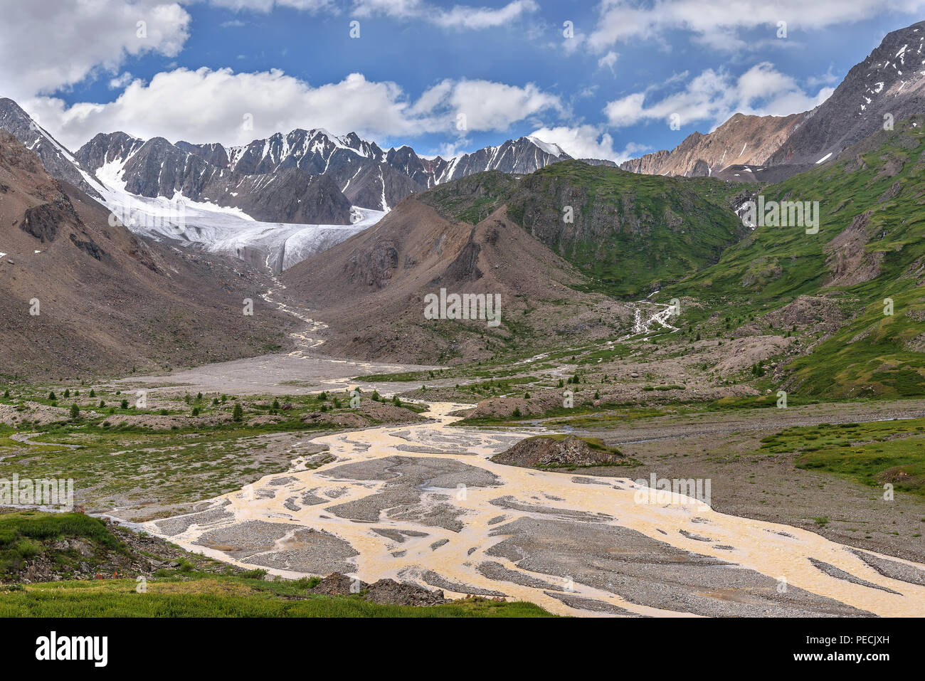 Amazing view on a beautiful glacier in the mountains, a green valley with a winding river, trees and stones against a background of blue sky and cloud Stock Photo