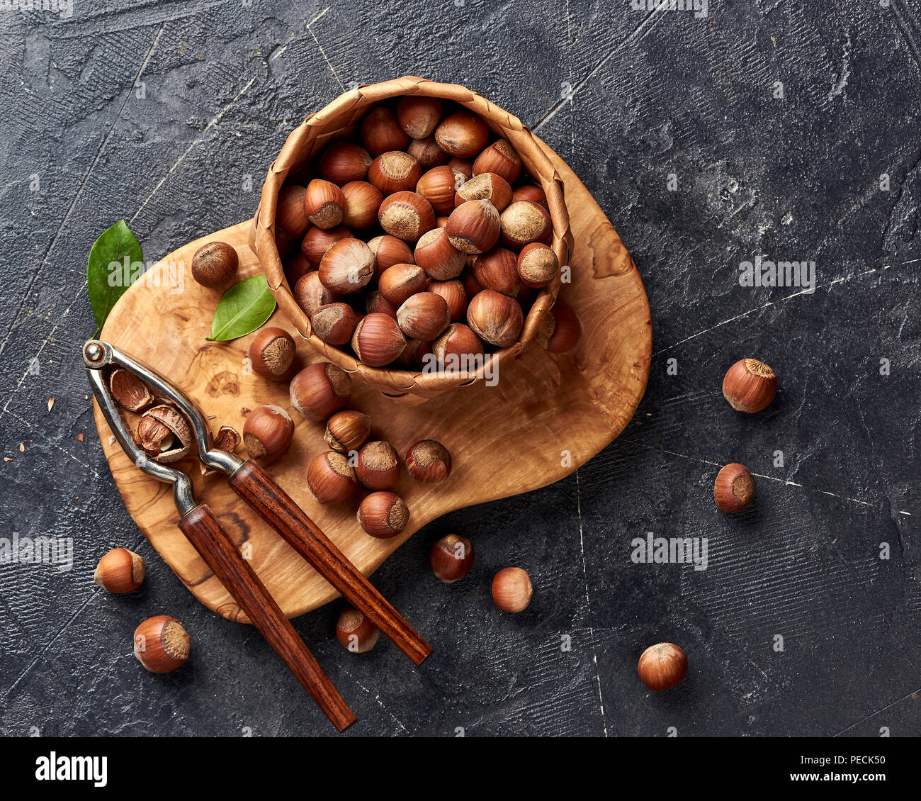 Hazelnut with nutcracker on olive wooden board. Nuts with green leaves. Top view. Stock Photo