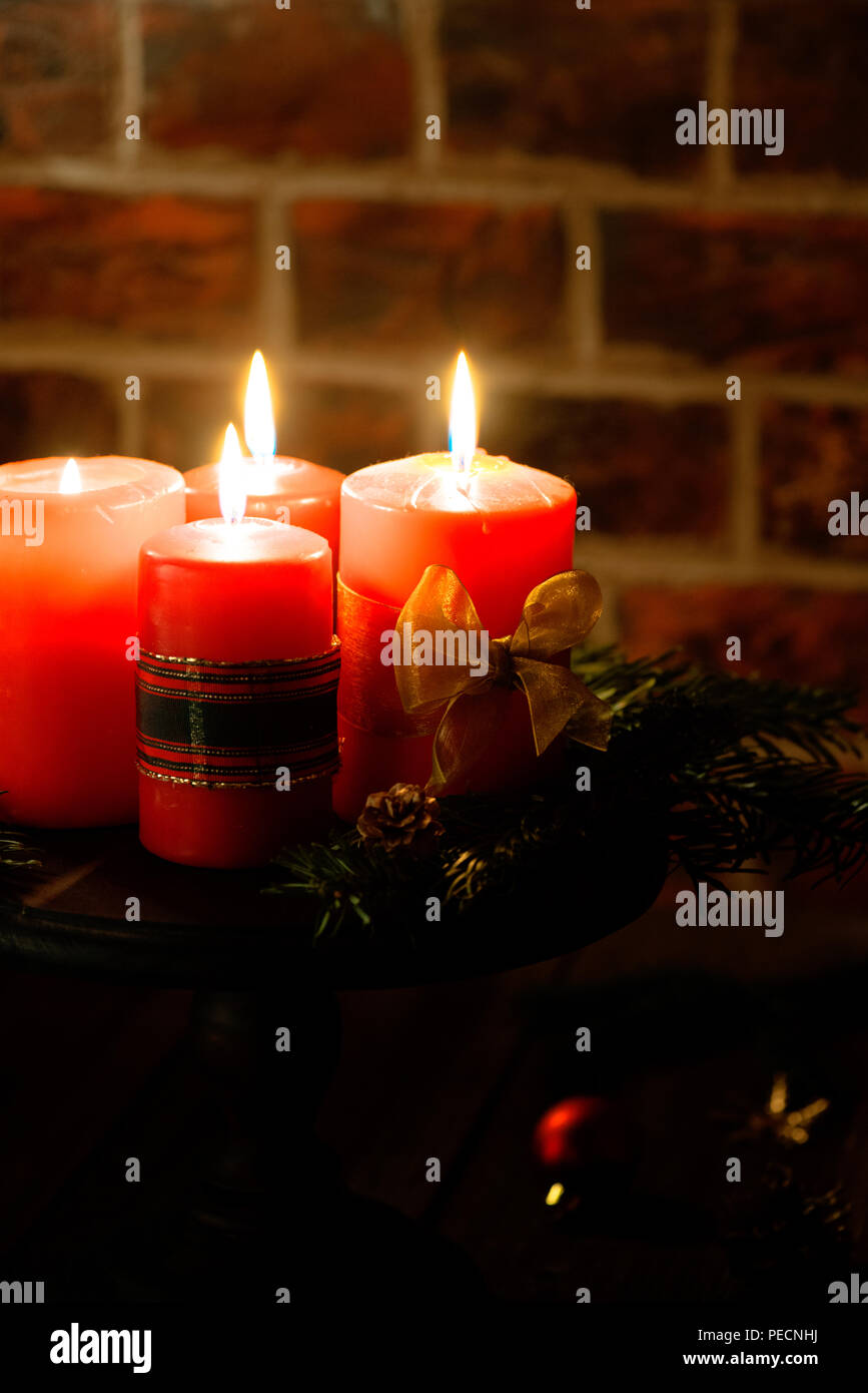 Four red candles with christmas decoration in atmospheric light. Moody. Authentic. Stock Photo
