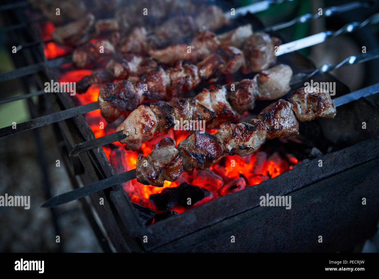 Grilling marinated shashlik preparing on a barbecue grill over charcoal.  Shashlik is a form of Shish kebab popular in Eastern Europe. Shashlyk (meaning  skewered meat) was originally made of lamb. Stock Photo