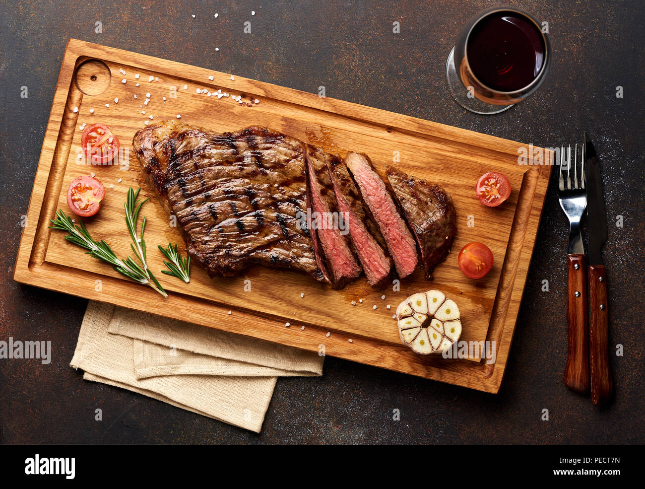 Grilled Black Angus Steak and a glass of red wine with tomatoes, rosemary on meat cutting board. Stock Photo