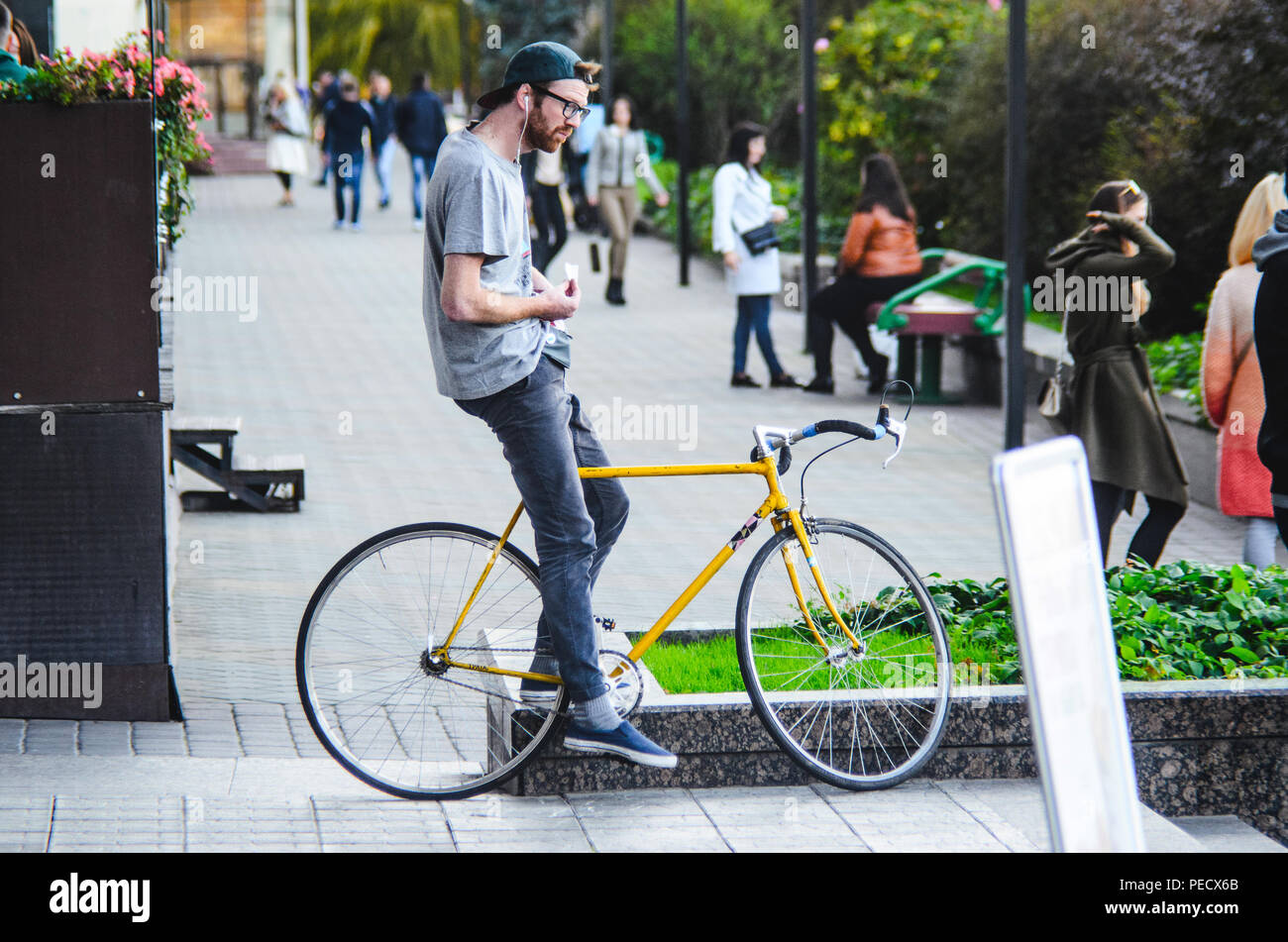 September 22, 2018 Minsk, Belarus: Young man stand with yellow fixie bike in cityscape and makes hand-roll cigarette Stock Photo