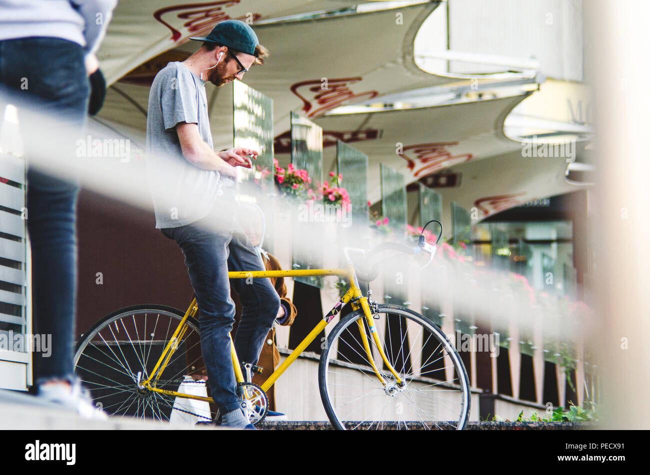September 22, 2018 Minsk, Belarus: Young man stand with yellow fixie bike in cityscape and makes hand-roll cigarette Stock Photo