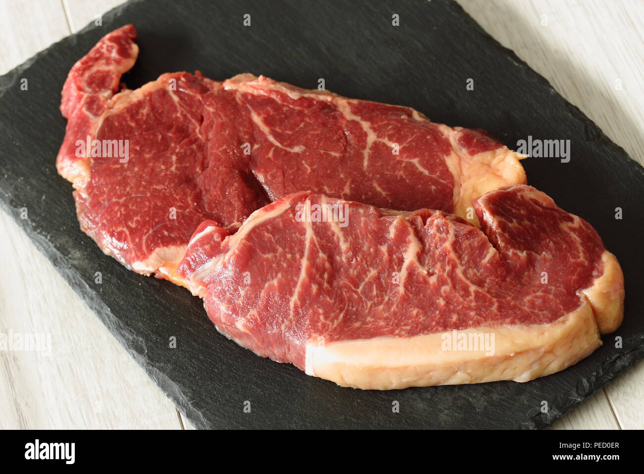Sirloin steak beef joints on a slate cutting board on a grey wood