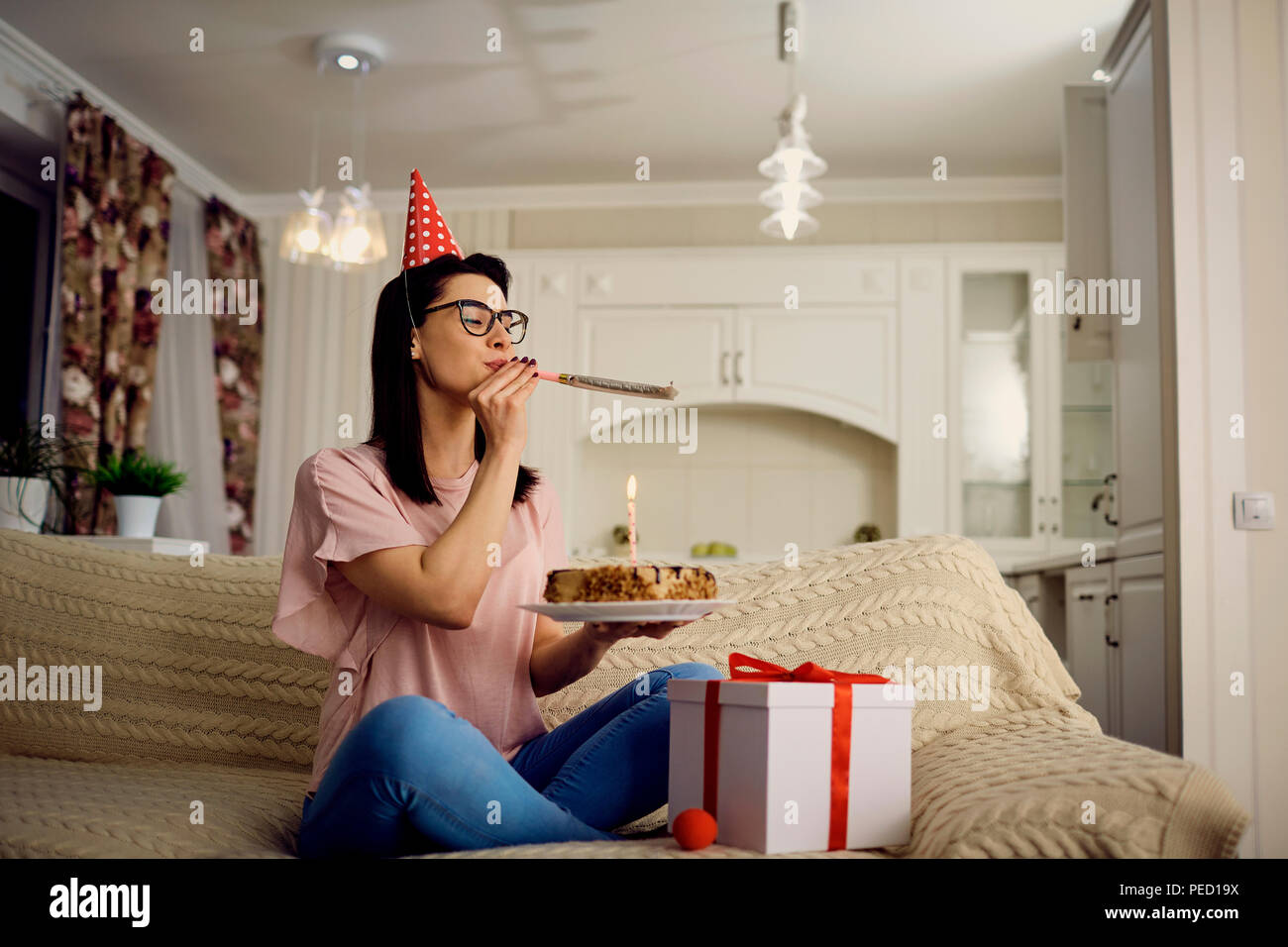 A girl in a cap alone with a cake with candles sitting on the so Stock Photo