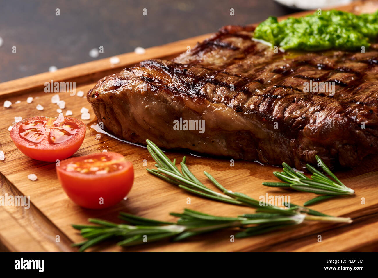 Grilled Black Angus Steak with tomatoes, garlic with chimichurri sauce on meat cutting board. Stock Photo