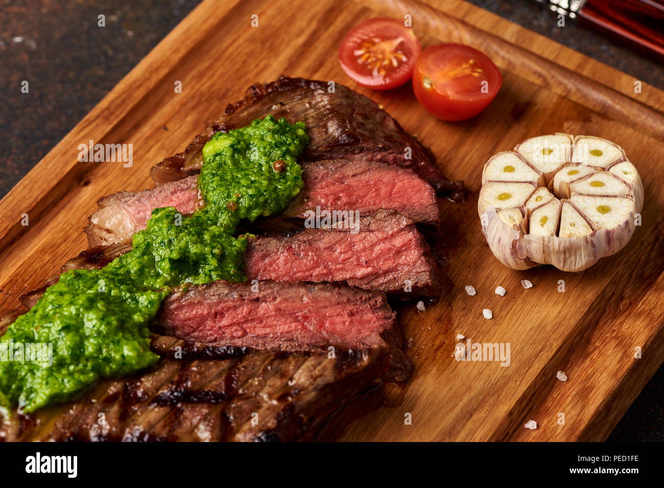Grilled Black Angus Steak with tomatoes, garlic with chimichurri sauce on meat cutting board. Stock Photo