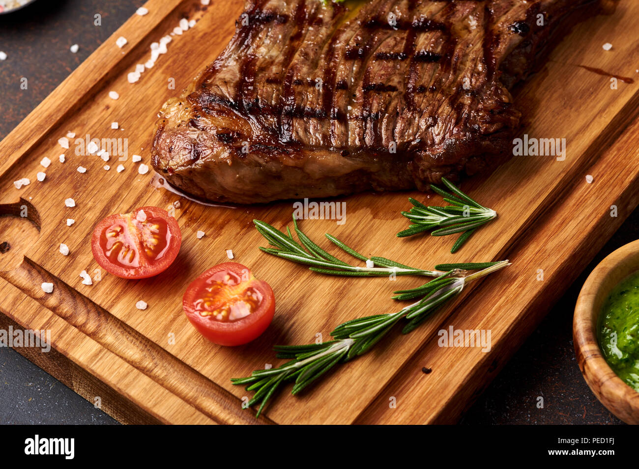 Grilled Black Angus Steak with tomatoes, garlic with rosemary on meat cutting board. Stock Photo