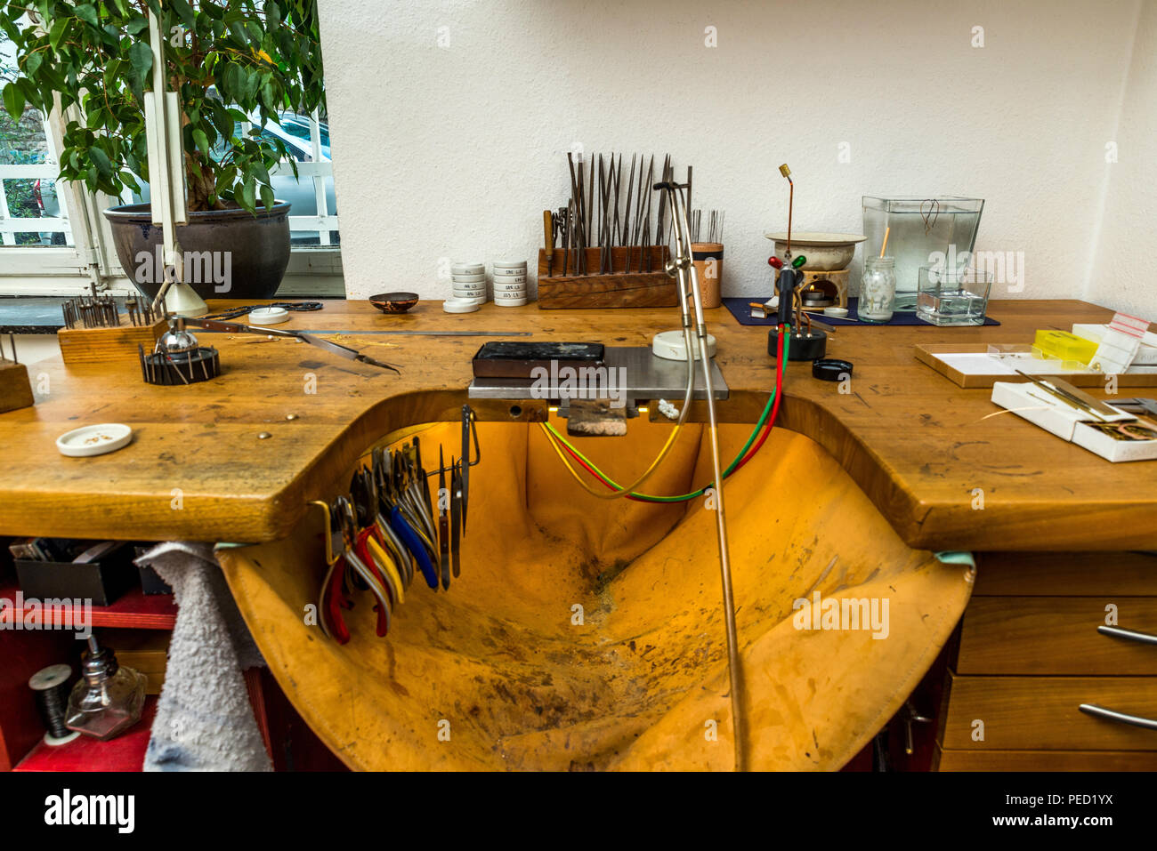 Equipment and tools of a goldsmith with polisher, tongs, pincers on wooden  working desk inside a workshop in the background Stock Photo - Alamy