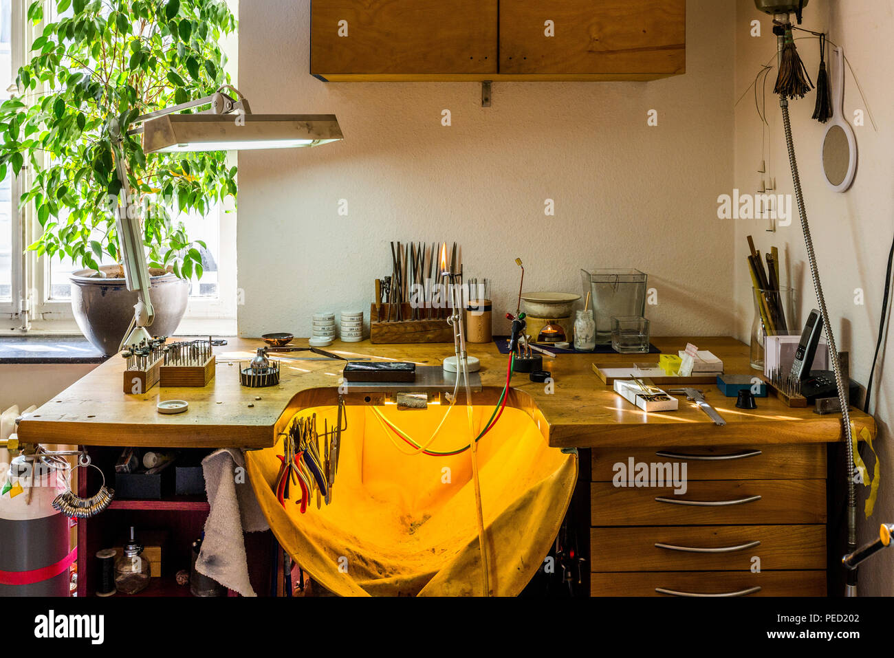 Equipment and tools of a goldsmith with polisher, tongs, pincers on wooden  working desk inside a workshop in the background Stock Photo - Alamy