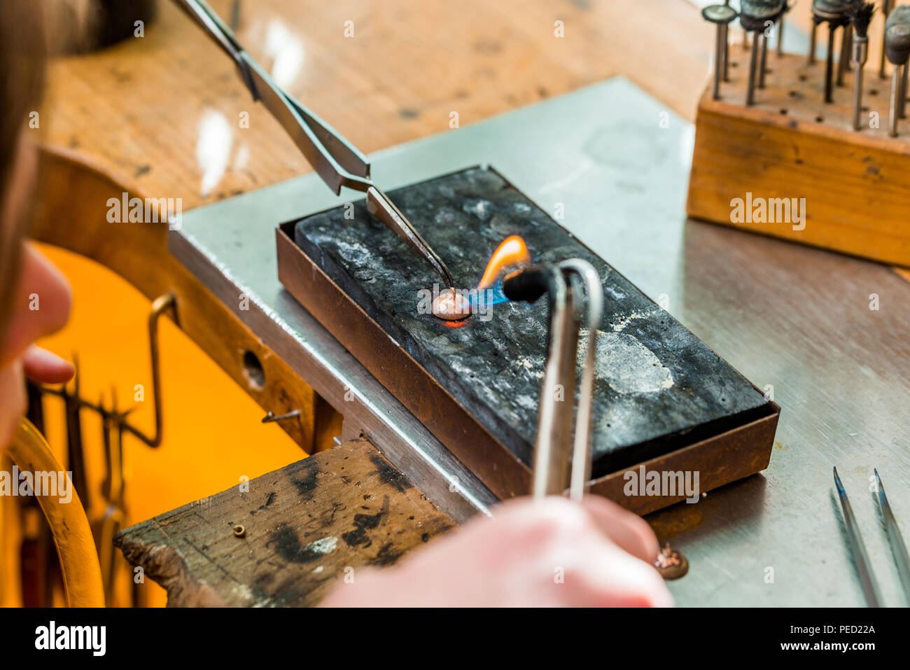 Goldsmith working and soldering an unfinished jewelry piece with a torch  flame at a workbench in workshop Stock Photo - Alamy