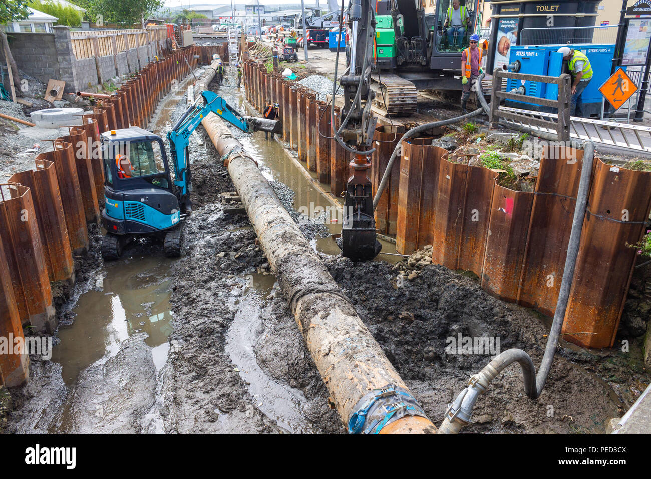 mini digger working on an excavation trench next to a pipeline next to metal shuttering. Stock Photo