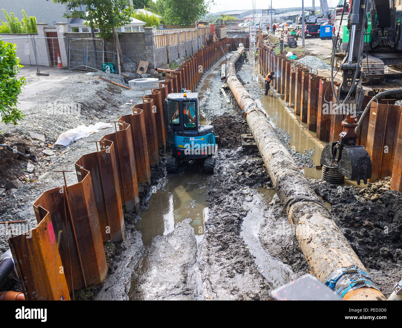 mini digger working on an excavation trench next to a pipeline next to metal shuttering. Stock Photo