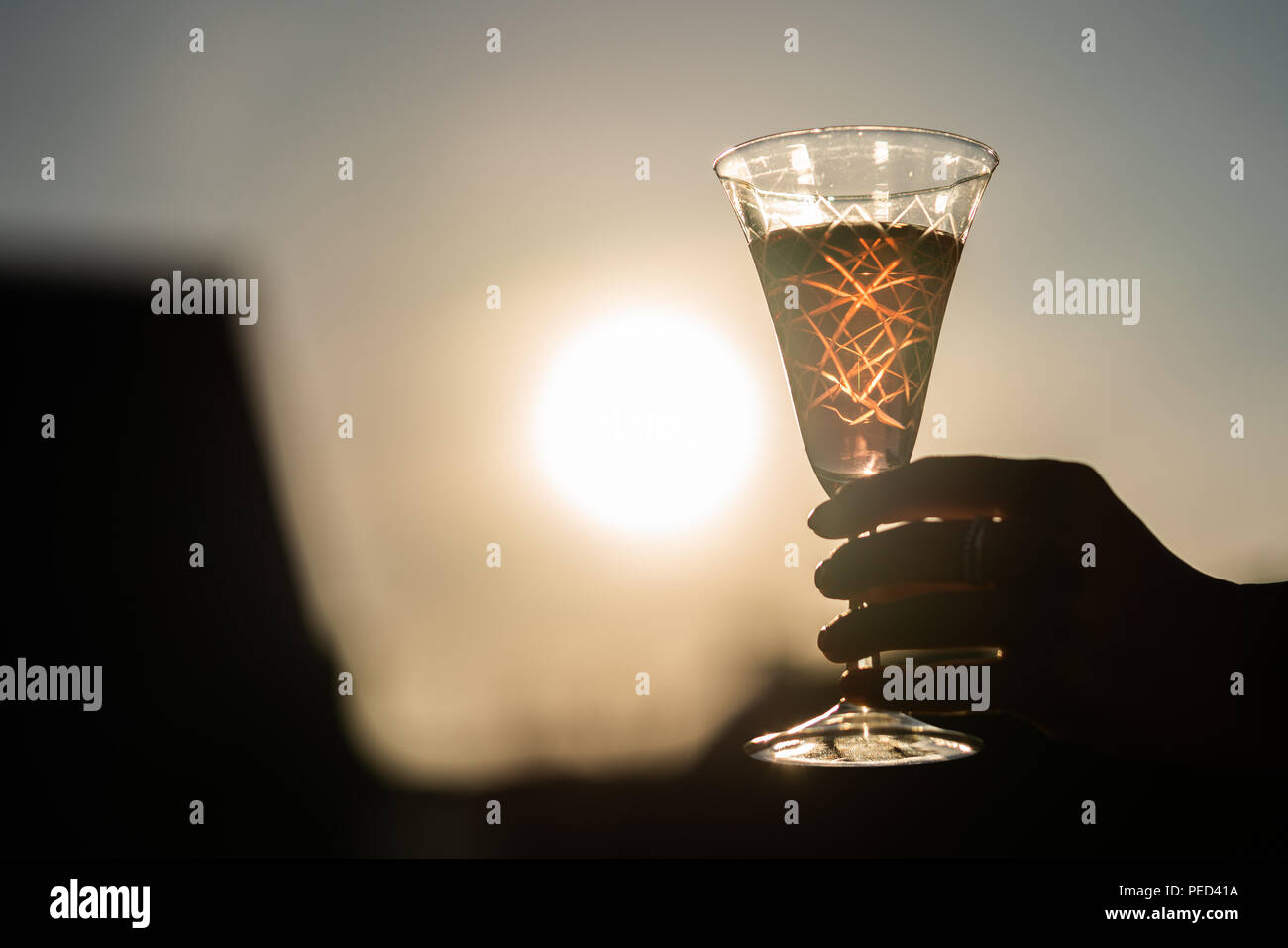 A glass of wine is being held by a woman right at the sunset. Stock Photo