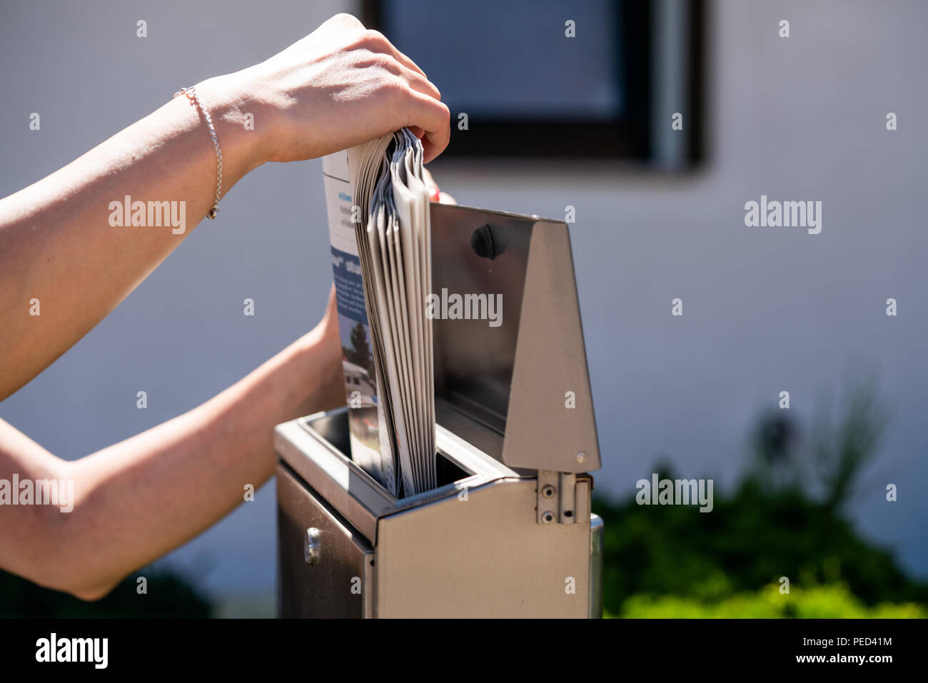 A woman takes a newspaper off a mailbox. Stock Photo