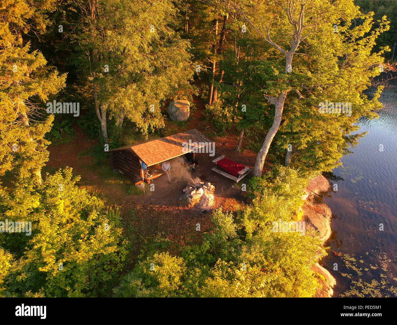 Aerial drone image of a Log cabin Lean-to shelter and campfire on a lake in the Adirondack Mountains. Bird's eye view of a waterfront campsite Stock Photo