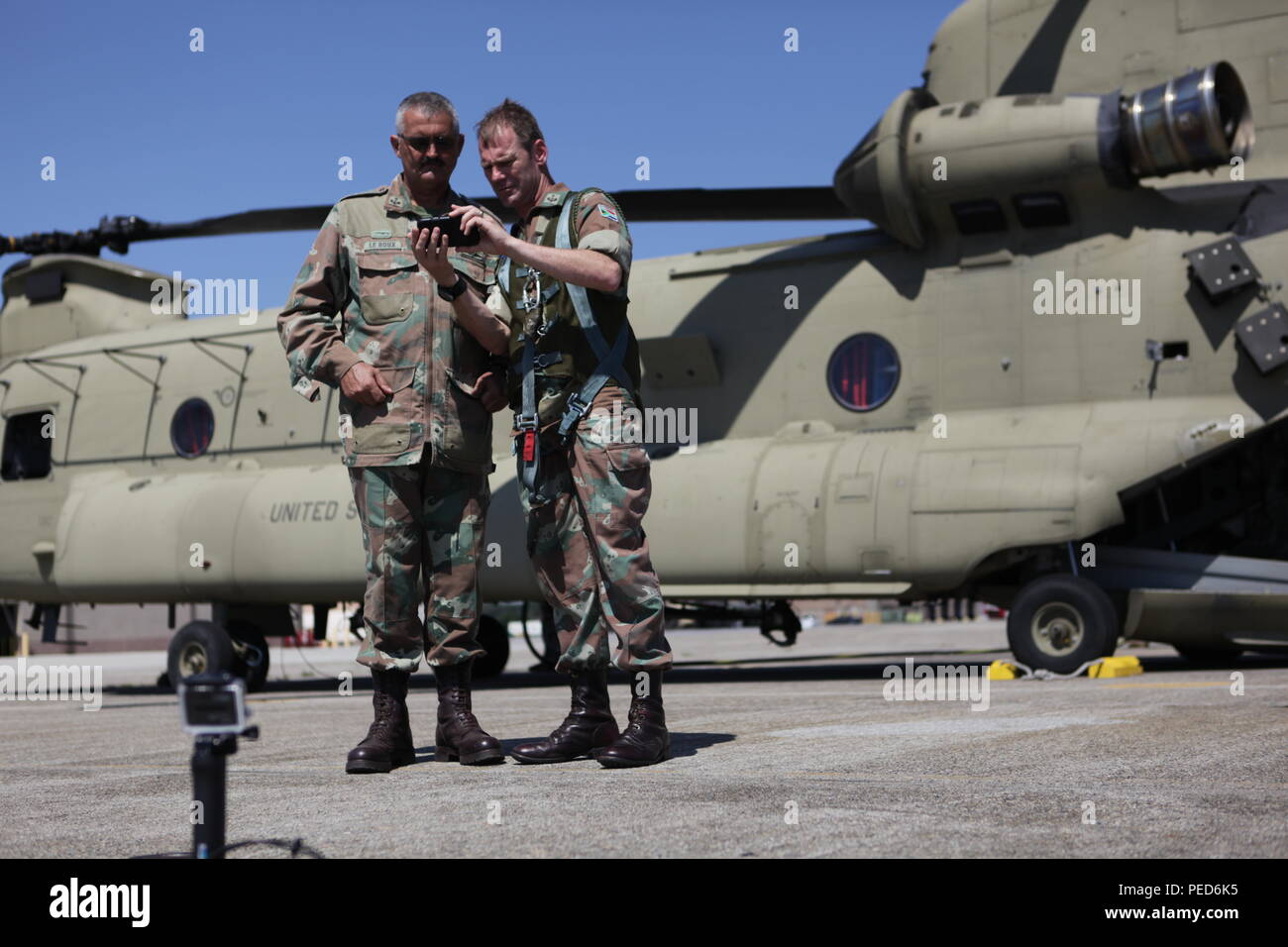 South African Lt. Cols. Laurel Thatcher and Skillie Le Roux look at images on a cell phone at Quanset Air National Guard Base while refueling a U.S. Army CH-47 Chinook for the international wing exchange jump, Aug. 3, 2015.  Leapfest is an International parachute competition hosted by the 56th Troop Command, Rhode Island National Guard to promote high level technical training and esprit de corps within the International Airborne community. (U.S. Army Photo by Sgt. 1st Class Horace Murray/Released) Stock Photo