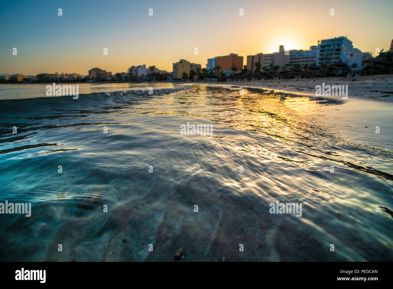 Golden waves of the sea and city on horizon during sunset Stock Photo