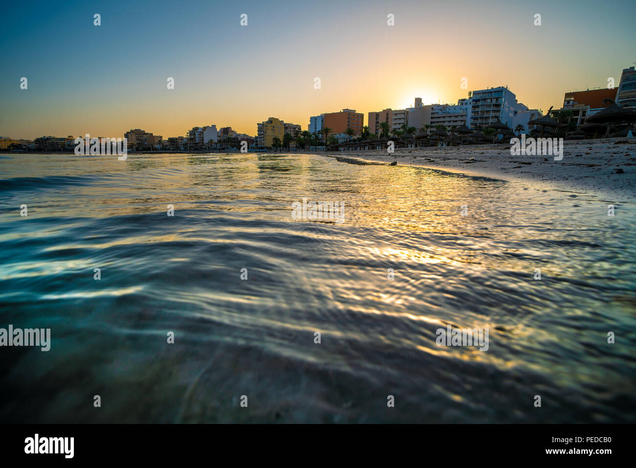 Golden waves of the sea and city on horizon during sunset Stock Photo