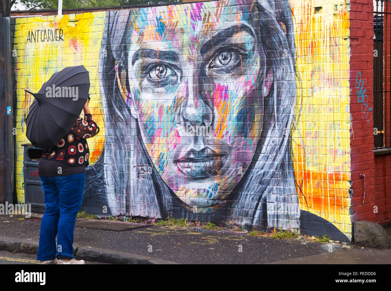 Woman with umbrella taking photo of street art of woman looking at Bristol on a wet rainy day in August Stock Photo