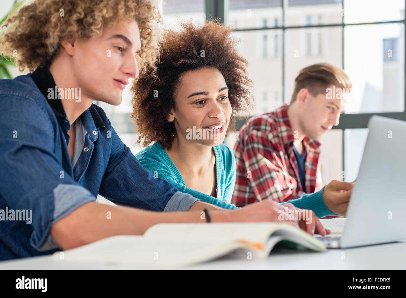 Cheerful woman writing an assignment while sitting between two classmates Stock Photo