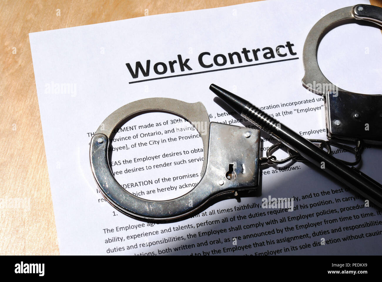 A pen, a pair of handcuffs on a written work contract waiting to be signed- Stock Photo