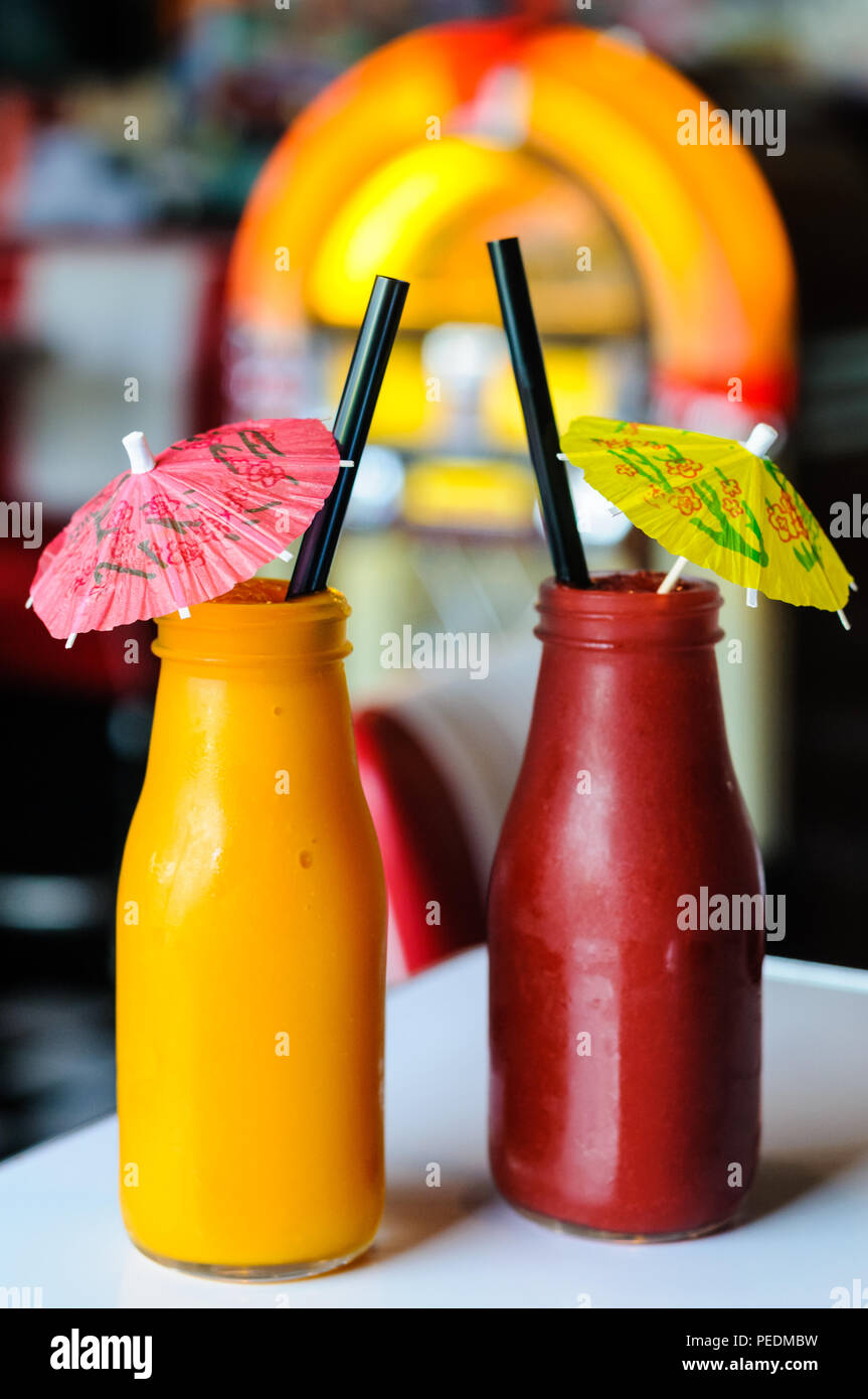 Two brightly coloured drinks with cocktail umbrellas in front of a jukebox Stock Photo
