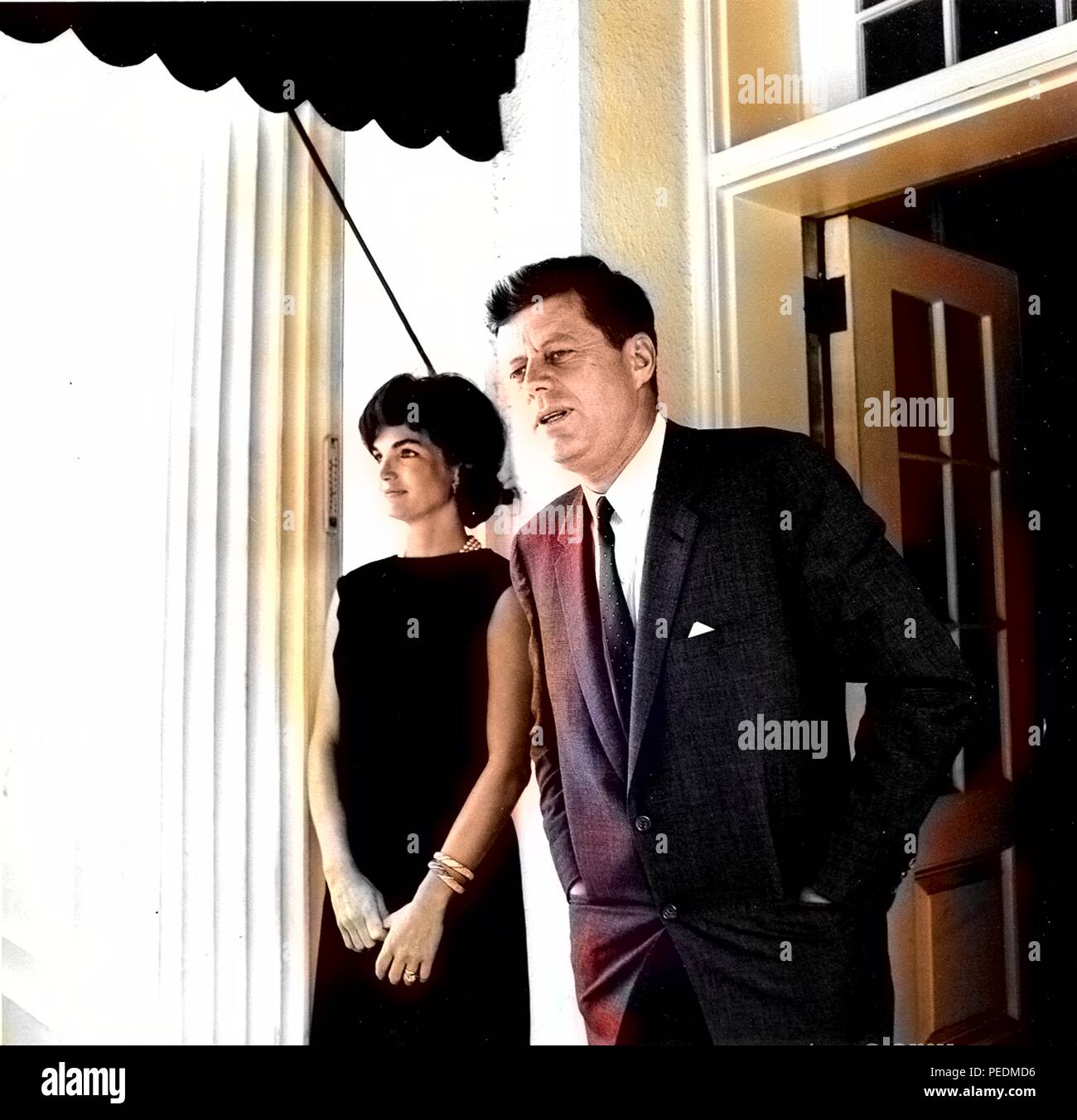 John F Kennedy and Jacqueline Kennedy stand together as they exit through a door at the White House, 1963. Note: Image has been digitally colorized using a modern process. Colors may not be period-accurate. () Stock Photo