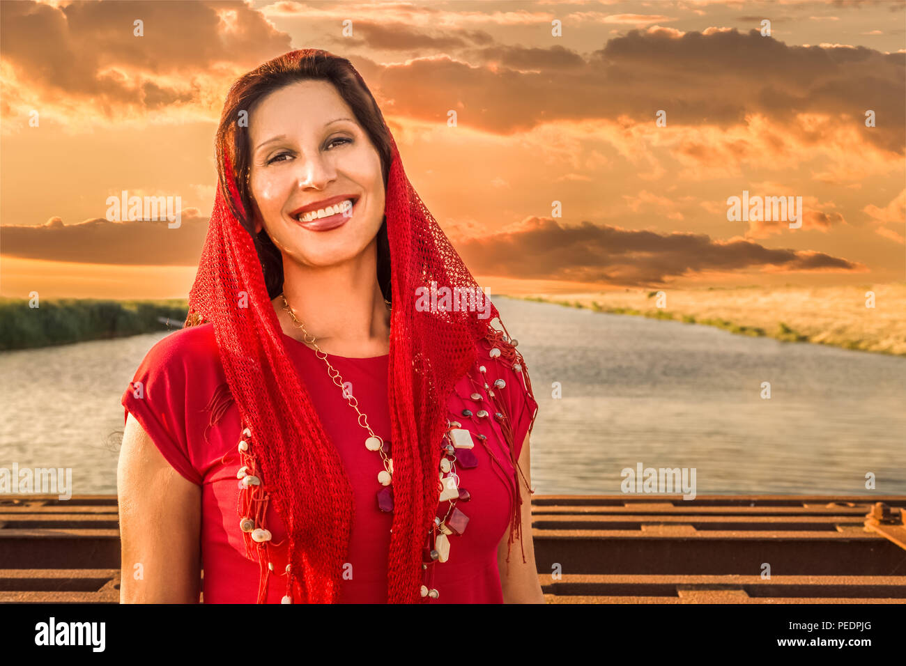 Mediterranean woman wearing red headscarf and smiling on river background Stock Photo