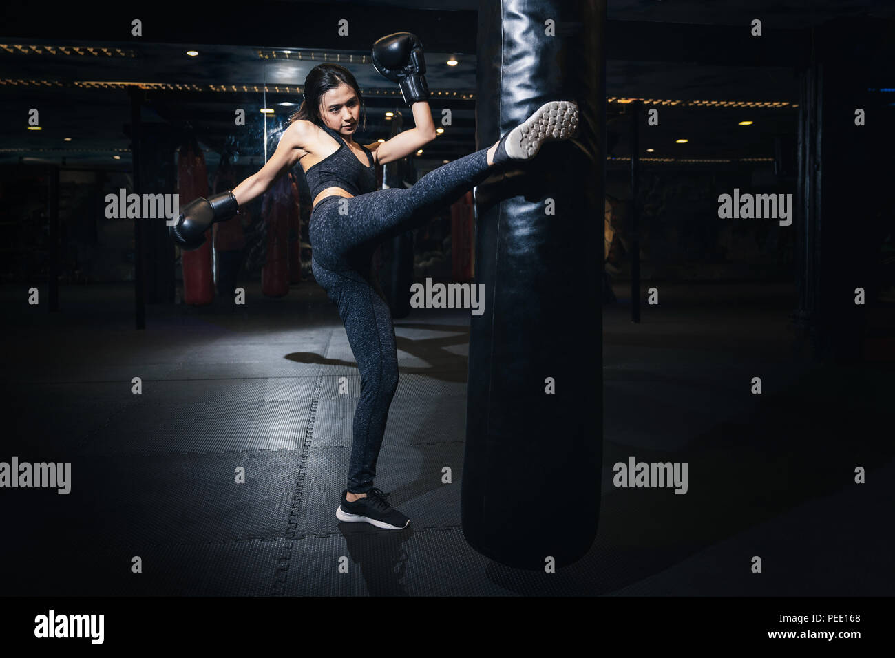 Female boxer hitting a huge punching bag at a boxing studio. Woman boxer training hard. Thai boxer punch kick by punching bag, Black bacground Stock Photo