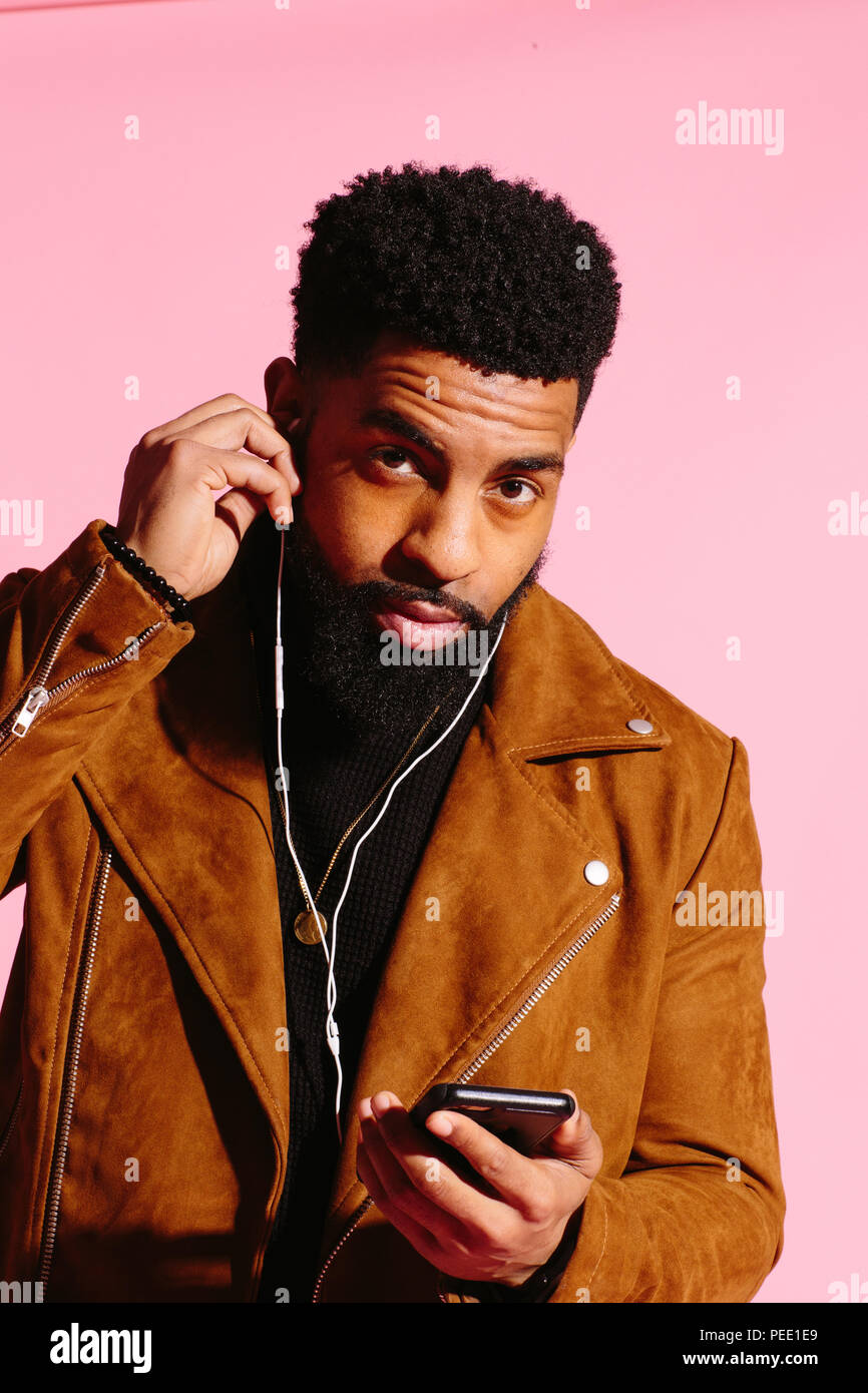 Cool African American man with beard, listening music, looking at camera, isolated on pink studio background Stock Photo
