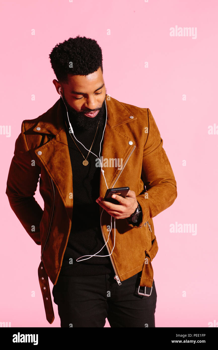 Cool African American man with beard, listening music, looking at phone, isolated on pink studio background Stock Photo