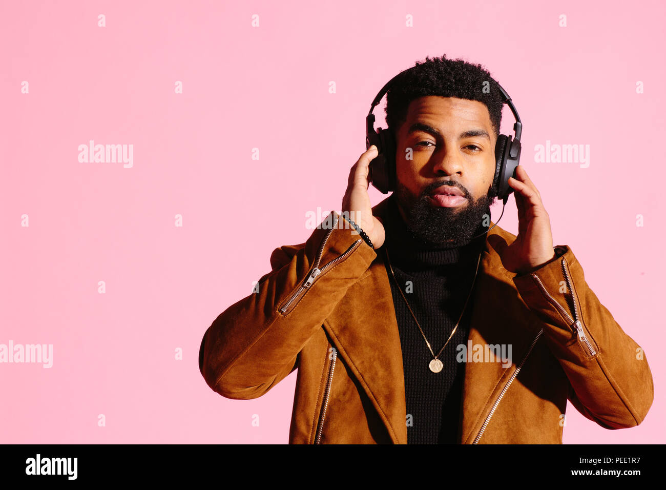 Handsome and cool African American man with beard, listening music, looking at camera, isolated on pink studio background Stock Photo
