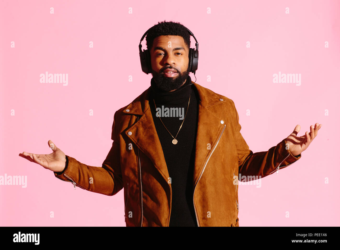 Cool African American man with beard, and headphones. isolated on pink studio background. Hands to the sides. Stock Photo