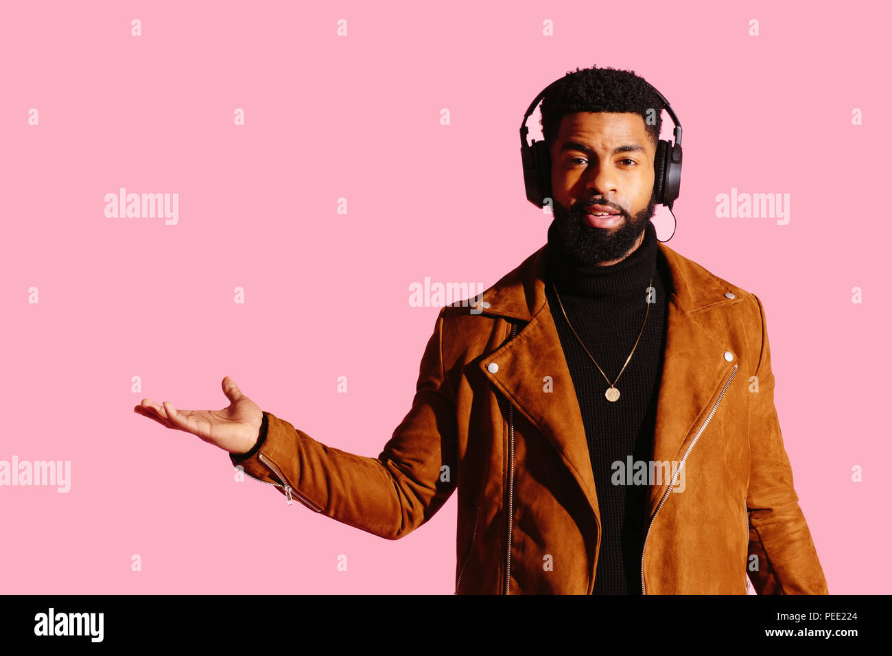 Portrait of a cool man with beard and headphones gesturing with his hand out isolated on pink studio background Stock Photo