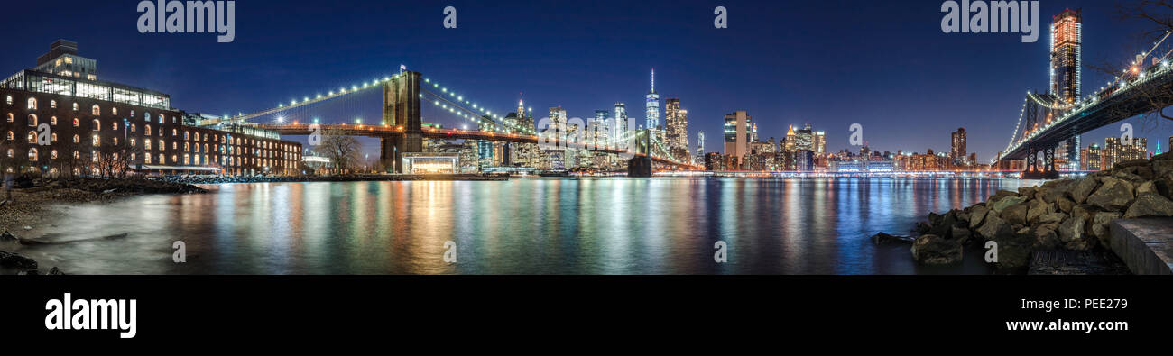 The skyscrapers of Lower Manhattan, the Brooklyn Bridge and the Manhattan Bridge in evening with the East River (panoramic). New York City Stock Photo