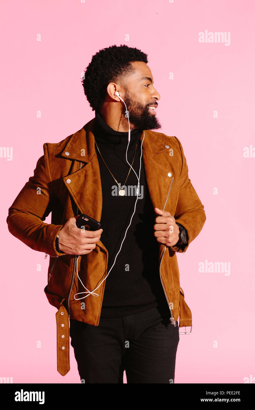 Stylish, handsome and cool African American man with beard, listening to music, isolated on pink studio background Stock Photo