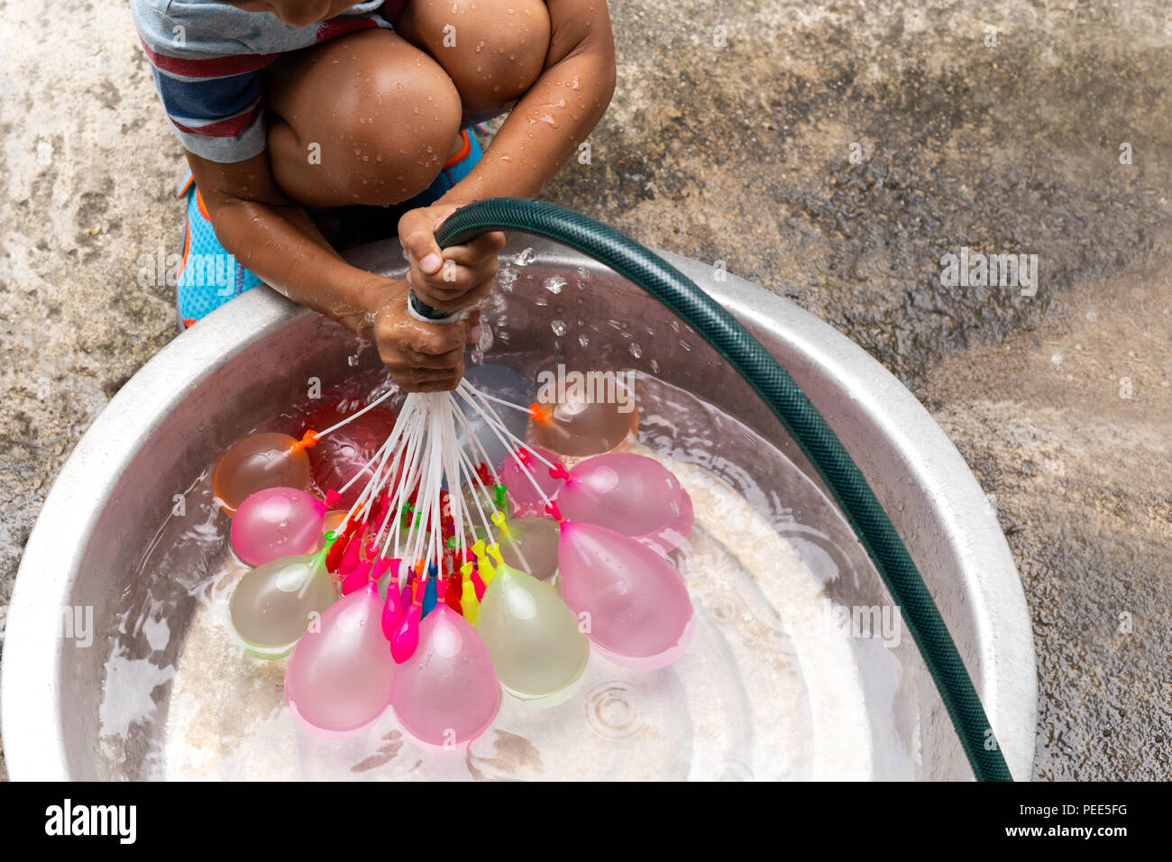 Little boy with water hose filling colorful water balloons in bucket